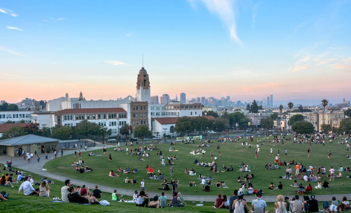 People sat on the grass in parkland overlooking the San Francisco skyline