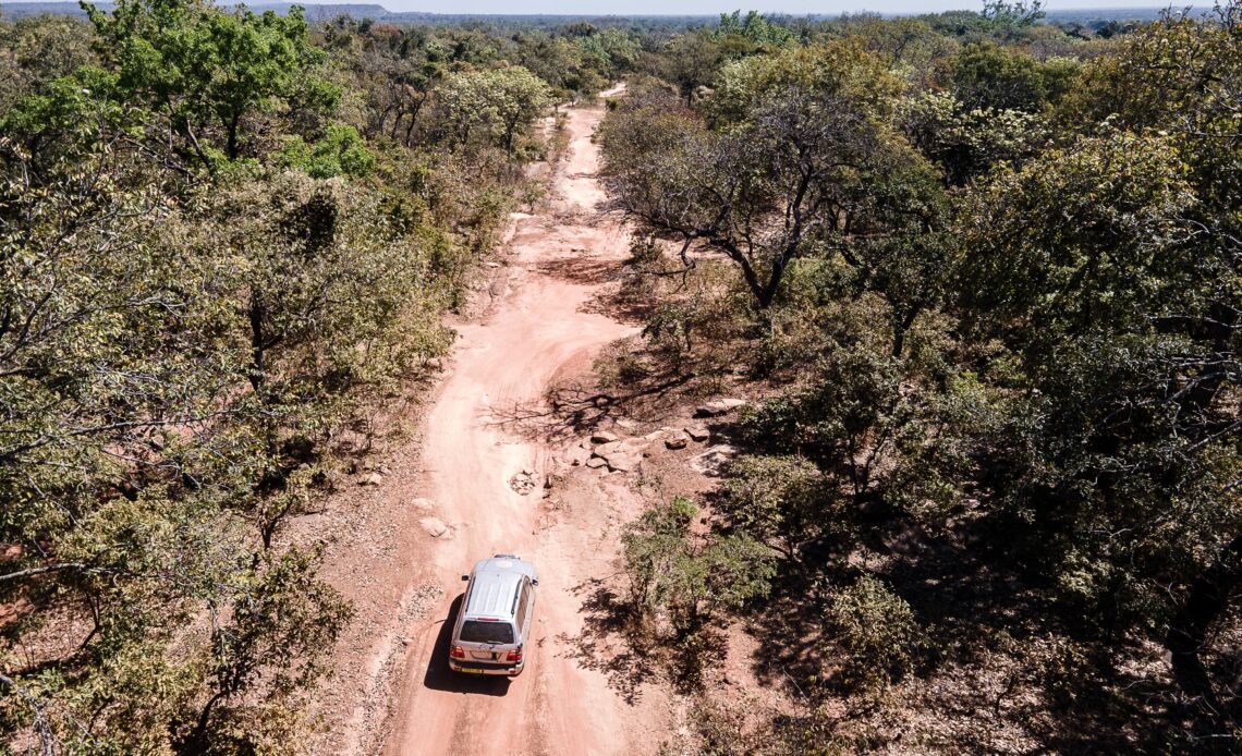 A jeep drives down a red dusty road between the trees.