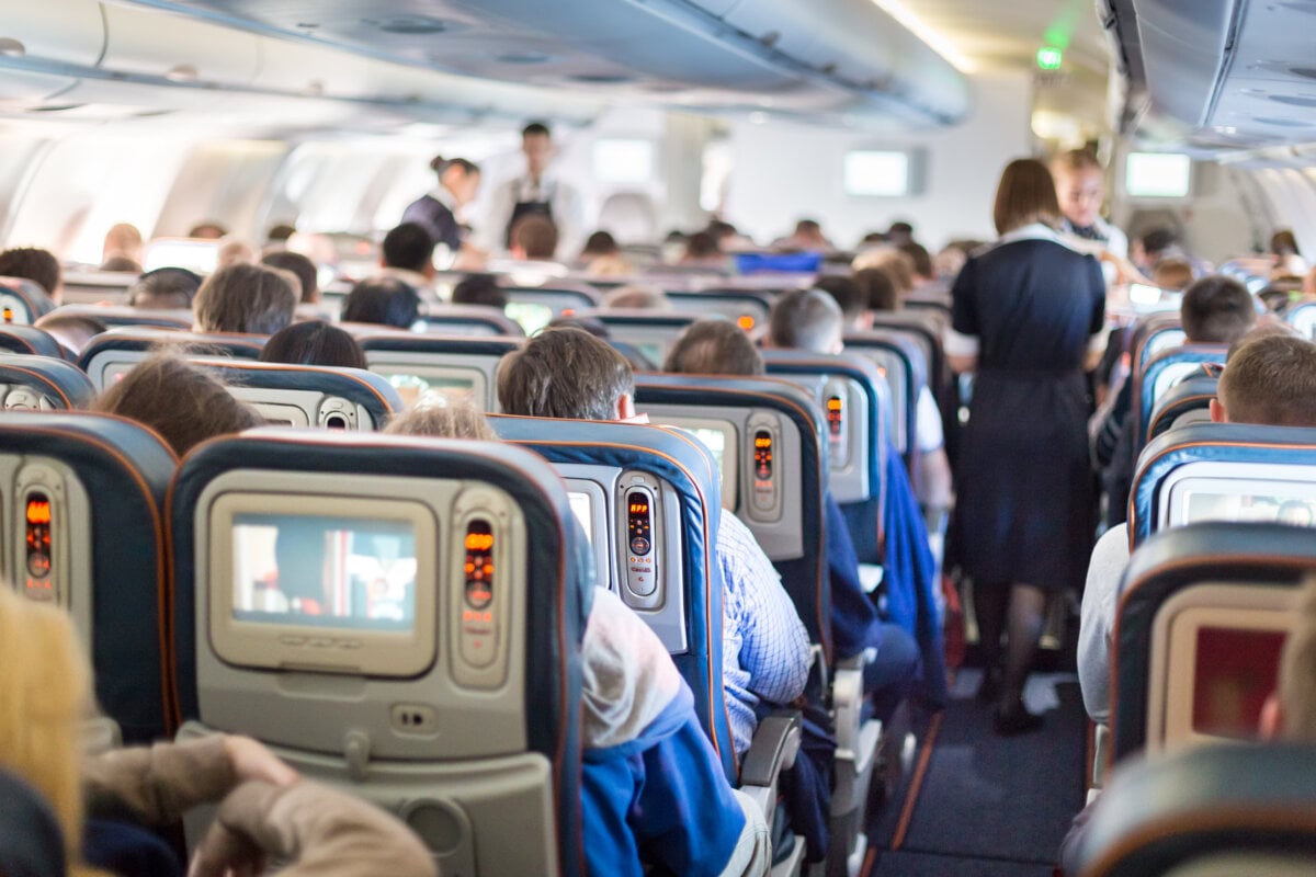 Interior of large passengers airplane with people on seats and stewardess in uniform walking the aisle