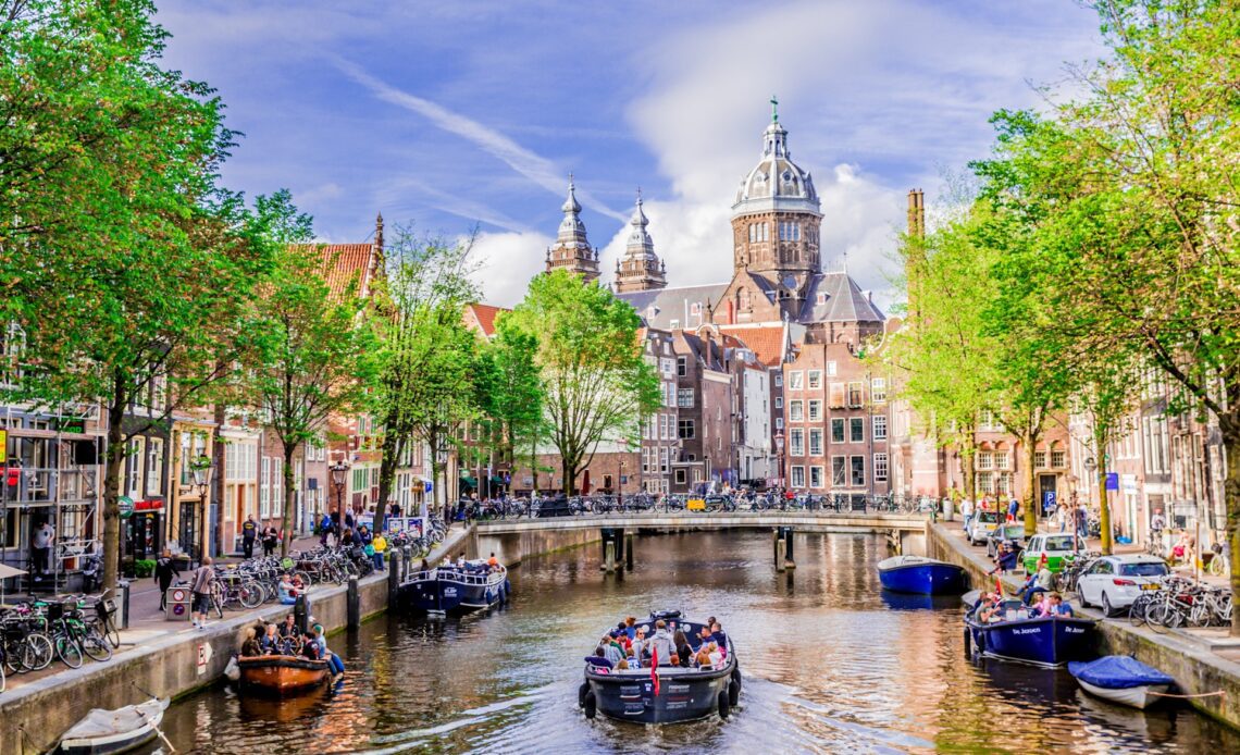 A small canal boat loaded with people moves along a canal in a city center