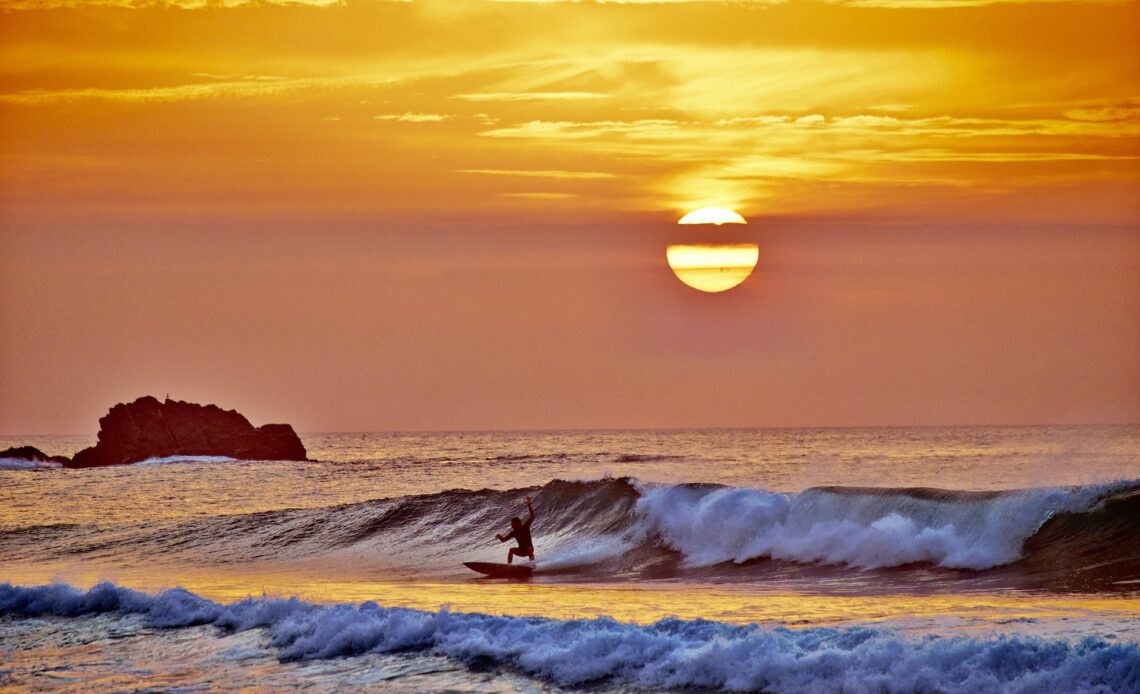 Sagres sunset above the Atlantic Ocean in Portugal with a surfer riding the waves