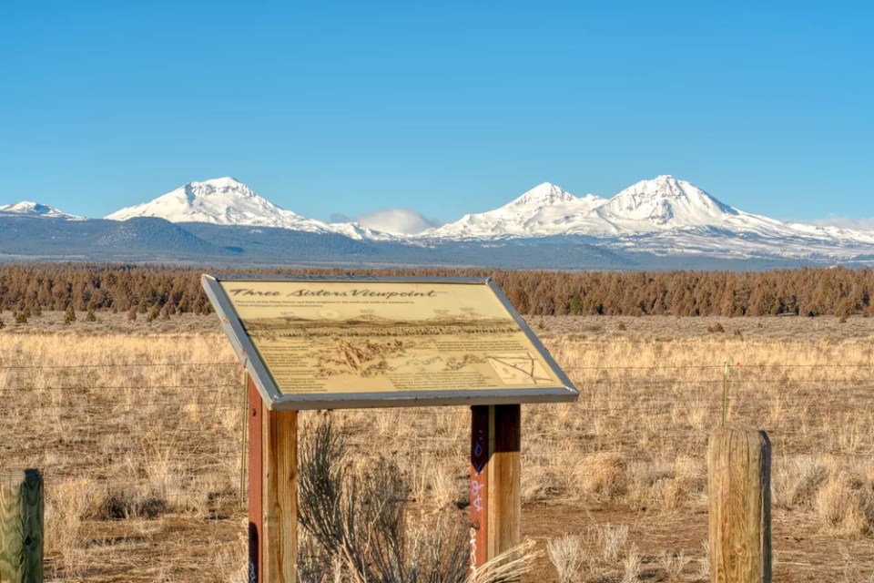 Three Sisters Mountains in Oregon with an informational sign.