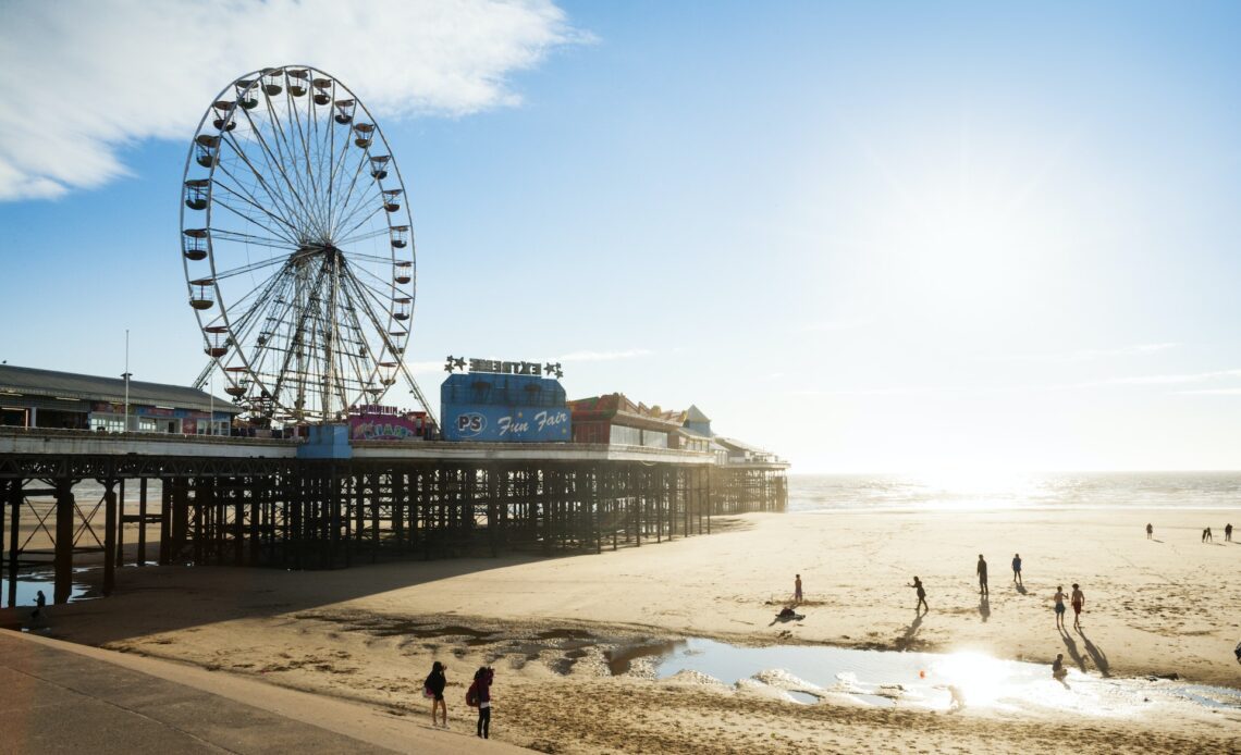 A Ferris wheel on a pier next to a broad sandy beach in the sunshine