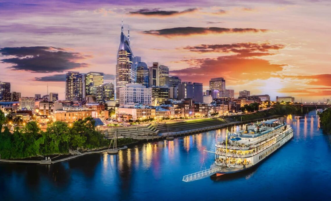 The skyline of Nashville, TN at dusk with an old boat cruising the river nearby