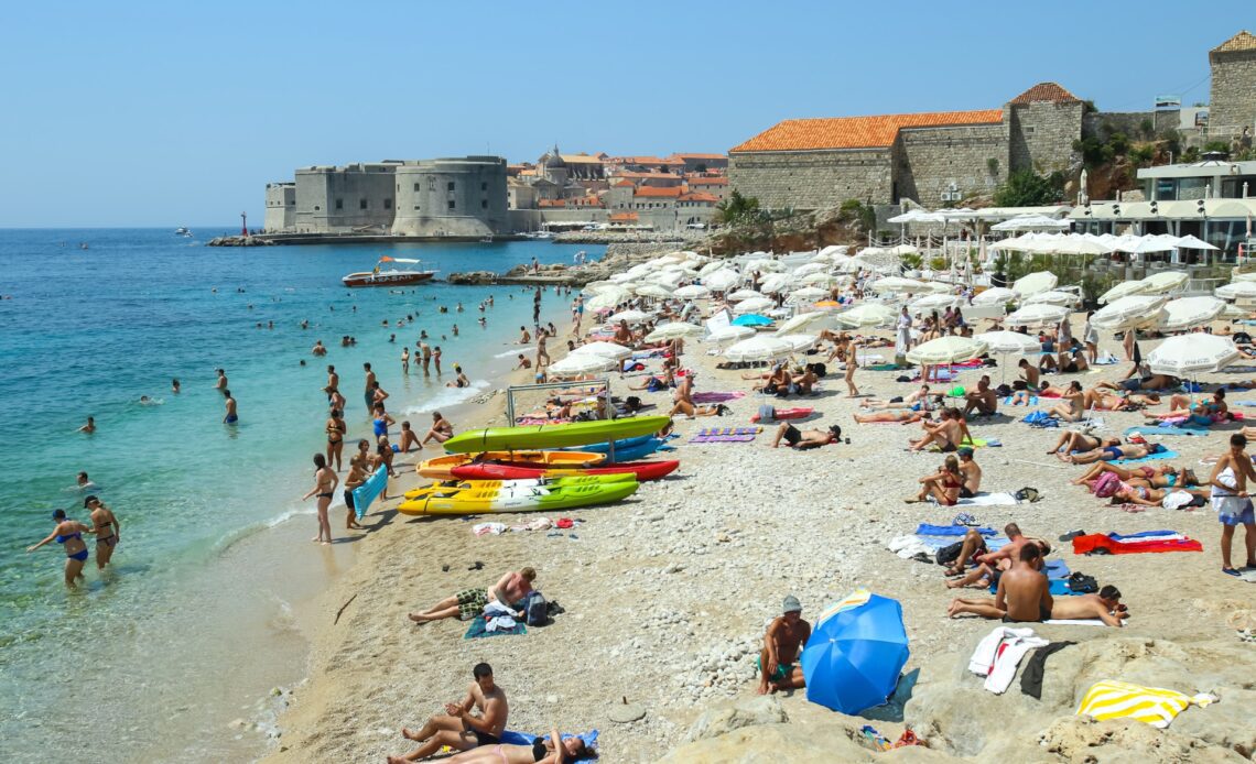 People swimming and sunbathing on the Banje Beach, with the old town of Dubrovnik in the background