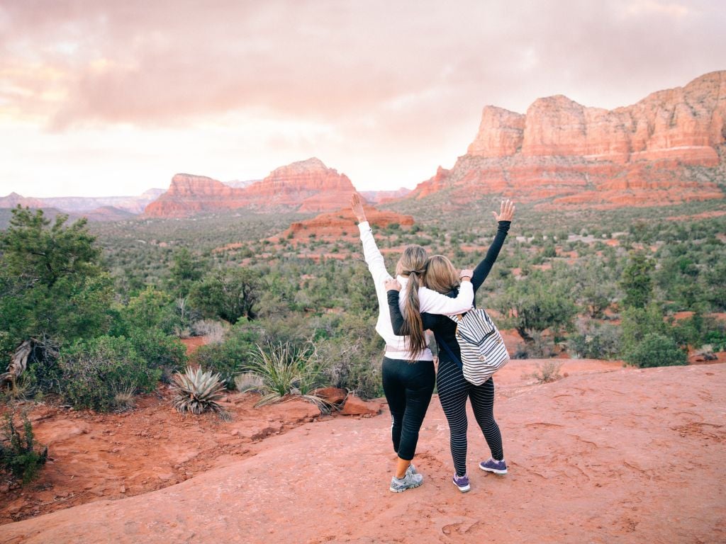 two women with their hands in the air in sedona arizona at sunset