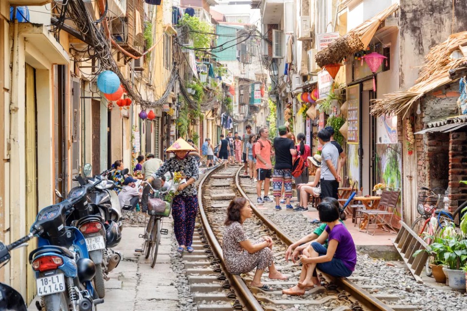 Vietnamese woman in traditional hat walking along a narrow street of the Hanoi Old Quarter. Tourists and residents waiting a passing train at the Hanoi Train Street.