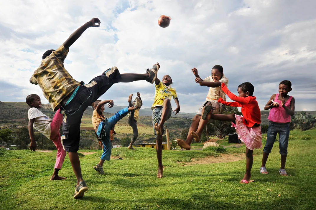 children play with a soccer ball on a grassy hill