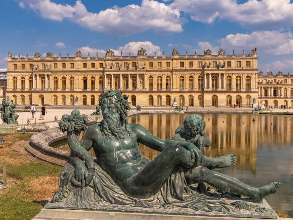 statue of man in front of pond in front of Versailles palace
