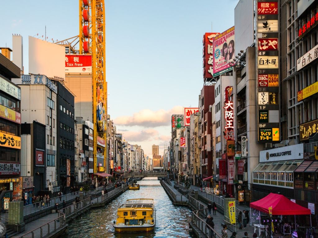 a river in osaka japan with a boat on it surrounded by tall buildings and billboards
