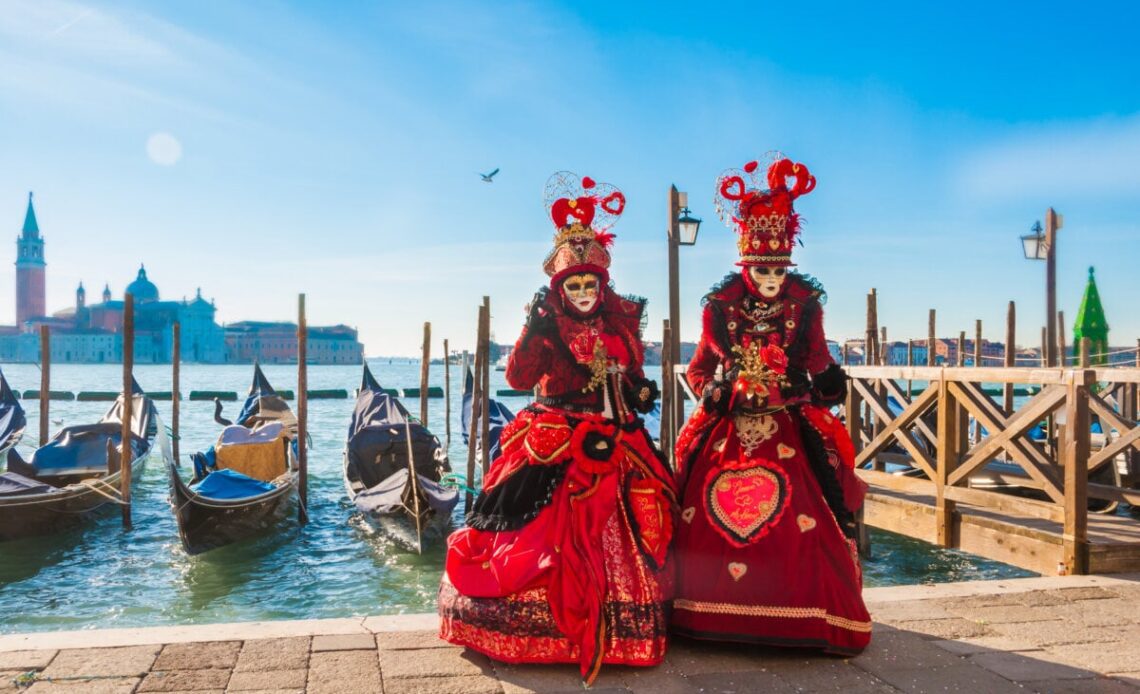 Couple wearing venitian carnival mask in front of gondolas in Grand Canal during Venice carnival in Italy