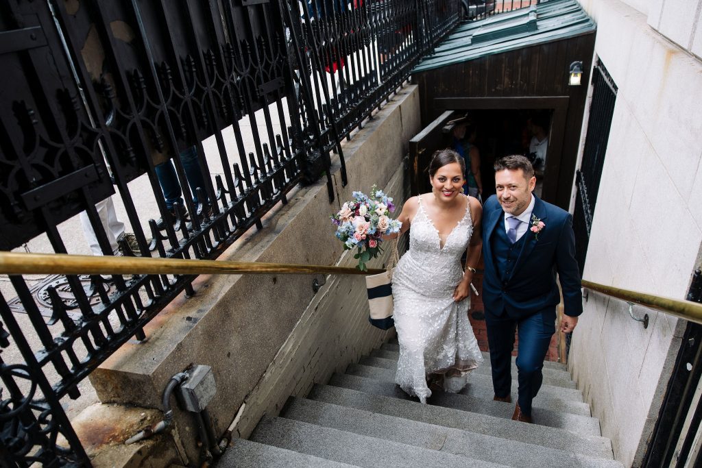 Kate and Charlie on their Boston wedding day, walking up the stairs from the basement bar Cheers. Kate holds her bouquet.