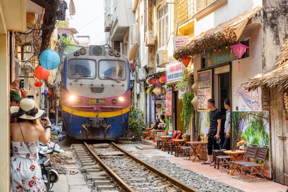 Incredible view of train passing through a narrow street, the Hanoi Old Quarter. Tourists taking pictures of the train. The Hanoi Train Street is a popular attraction.