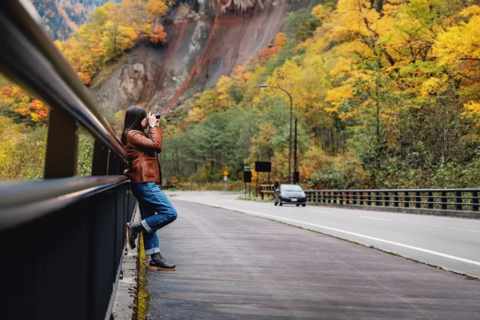 Travel Concept. Young Traveling Woman with Camera taking Photo in Fall and Autumn Nature Scenery