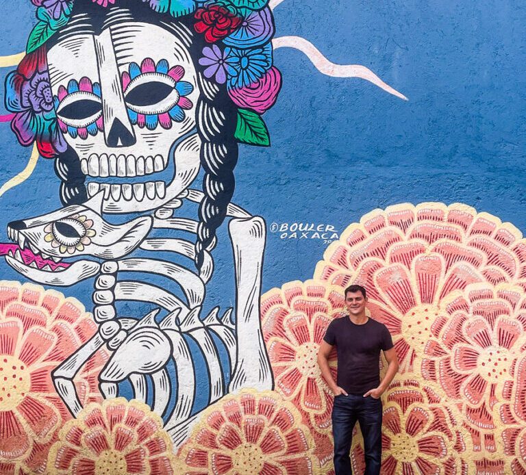 Matt Kepnes standing next to a mural in Oaxaca, Mexico
