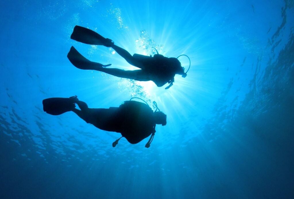 two people scuba diving with sun beaming in from above