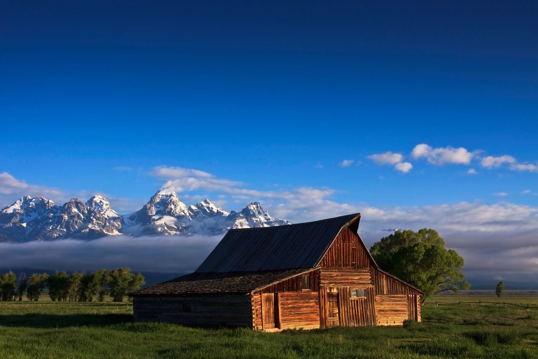 a barn sits in the foreground with mountains in the distance
