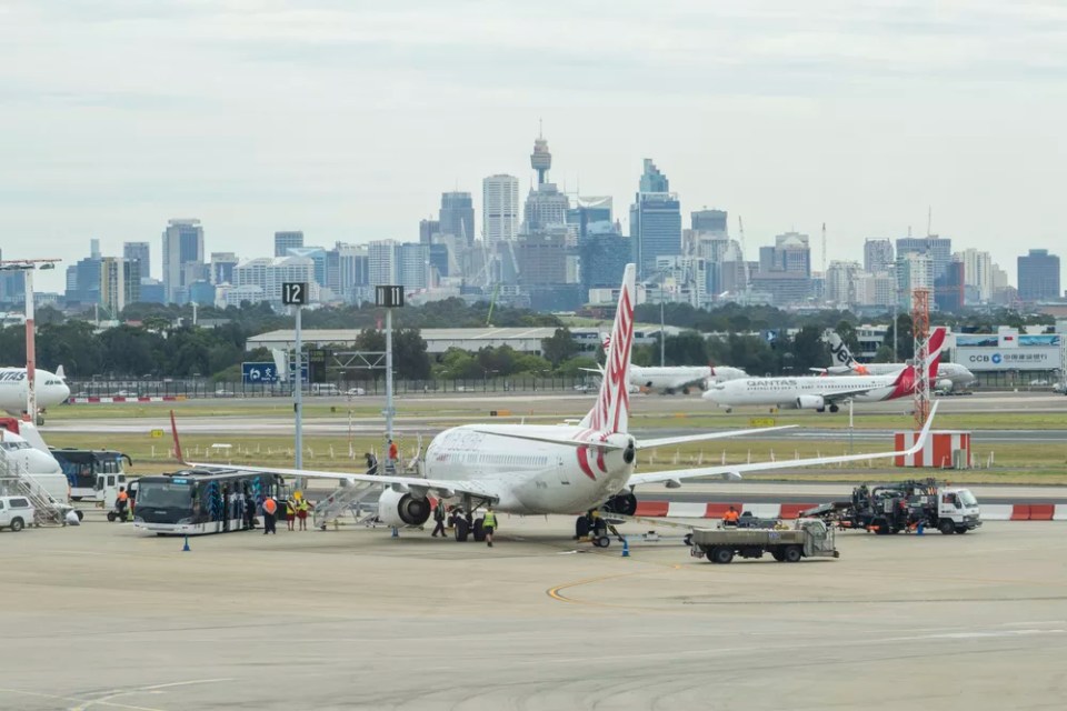 View of passengers getting off an airplane at the Sydney Airport, with view of CBD in the background. It is the busiest airport in Australia.