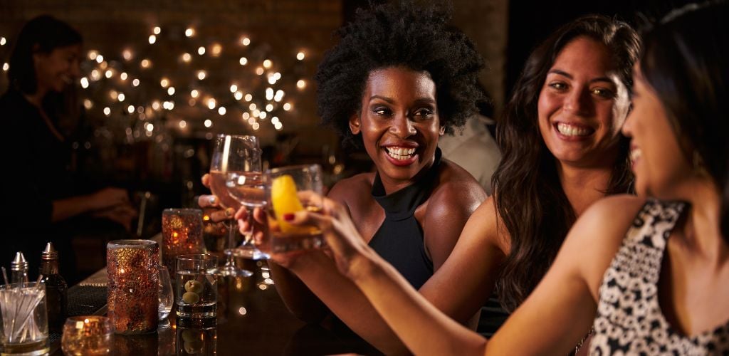 Three women at the bar with wine and champagne glasses.