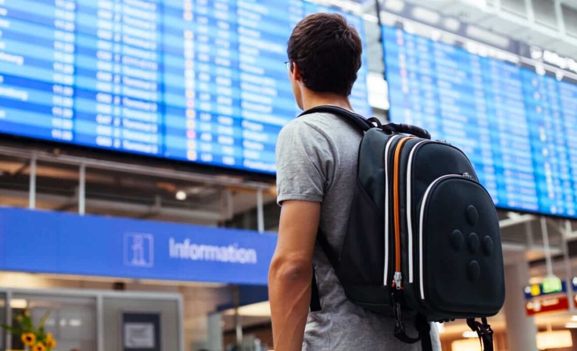 Young man with backpack in airport looking at a flight timetable