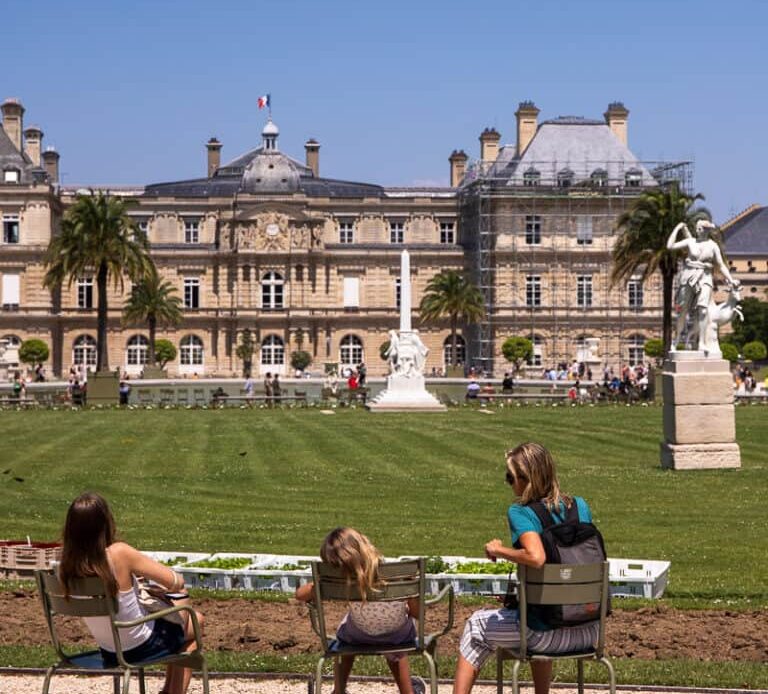 caz and girls sitting on chairs looking at palace in luxembourg gardens