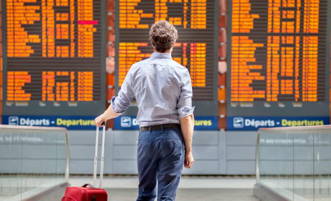 A man standing beside his luggage looking at an airport flight board