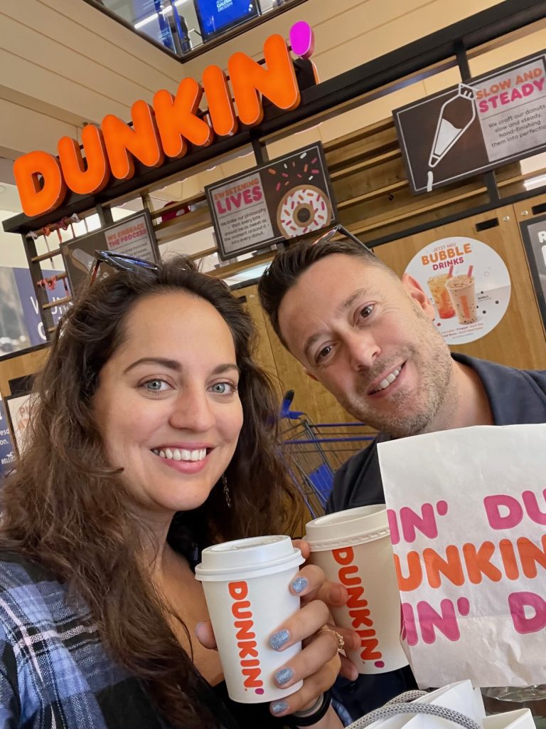 Kate and Charlie take a smiling selfie at Dunkin', holding up Dunkin-branded coffee and donuts.