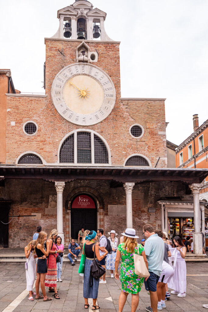 group of people standing in venice square in front of Chiesa di San Giacomo di Rialto