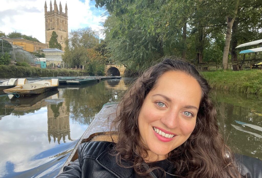 Kate takes a selfie while on a boat in the river in Oxford, a castle tower in the distance behind her.