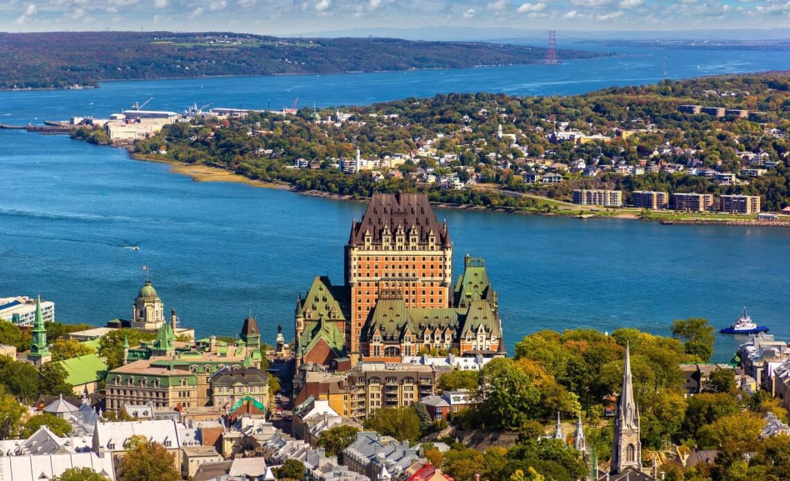 Panoramic aerial view of Quebec City in Canada, with Frontenac Castle as a prominent feature of the skyline and the deep blue of the Lawrence River in the background