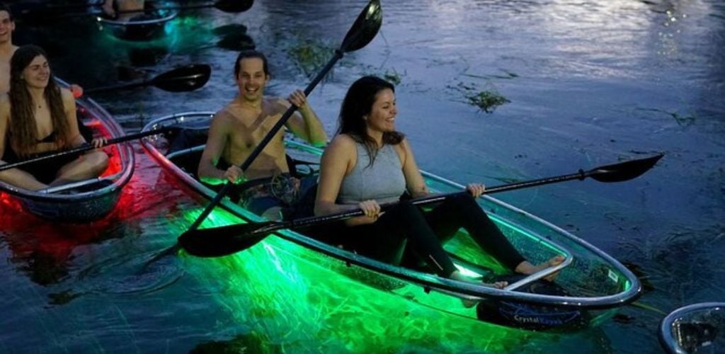 A happy young adult couple kayaking using a Neon Night Glow Clear Kayak.