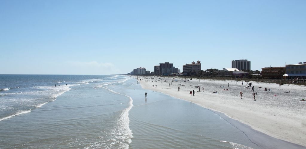 A beach and tourists at the shore and a building in the background.