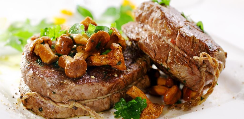 Meat a stake on a plate close up with mushrooms on the top.