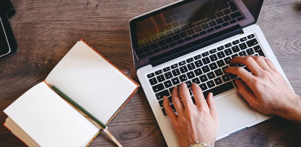 Open notebook on a wooden table, a wristwatch and a pen, analog camera, a laptop. Writer's setup, seeking inspiration or just a quick note.