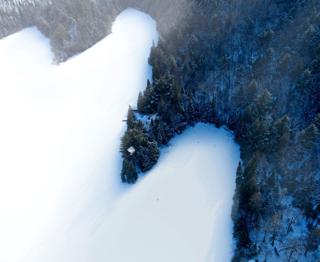 a tree lined frozen lake shown from above