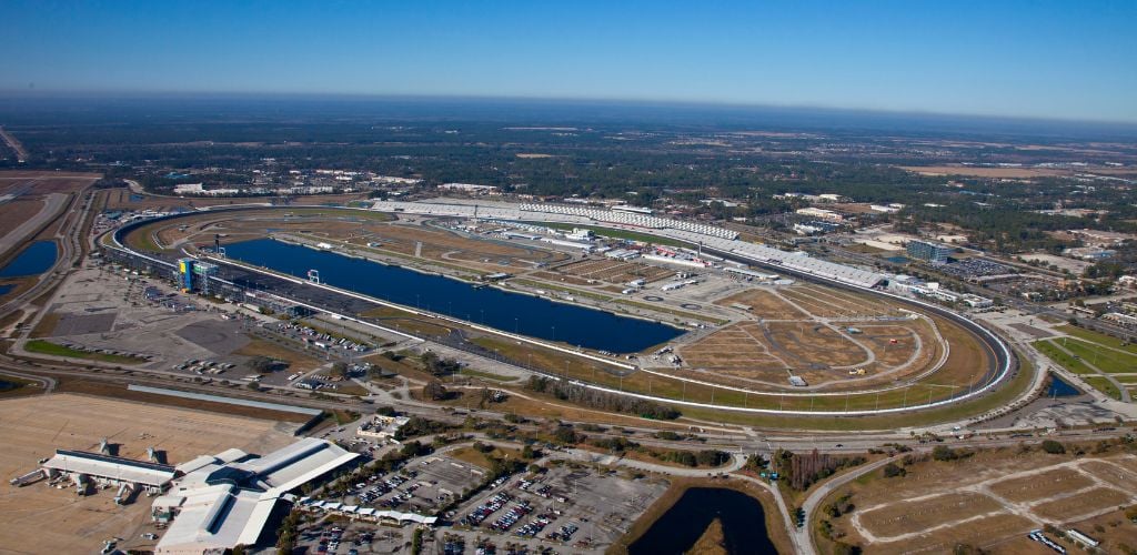 Aerial view of Daytona International Speedway in Florida. There is a parking lot, as well as little lakes and open space.