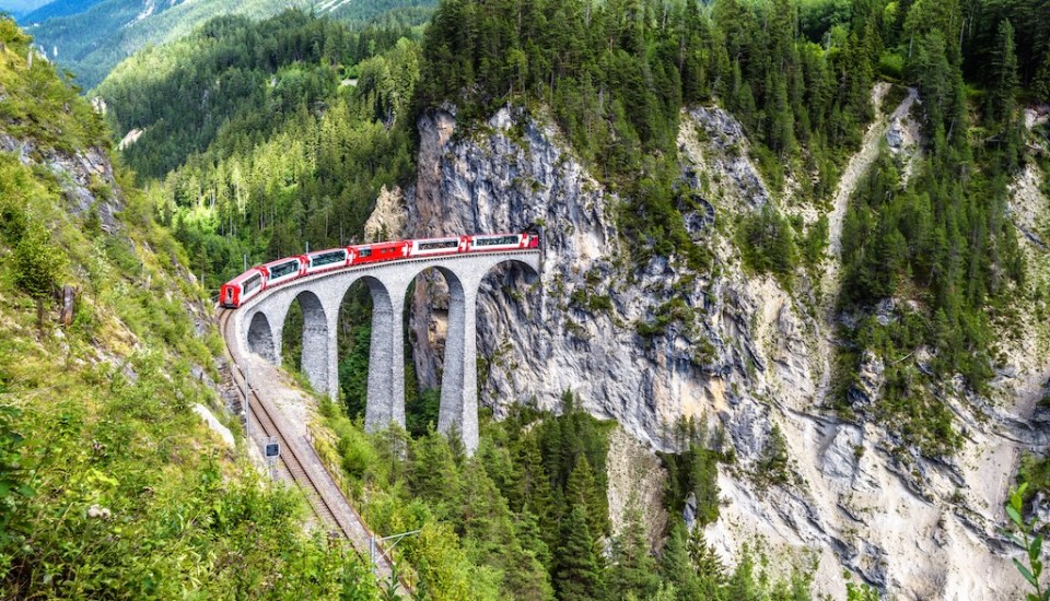 Landscape with Landwasser Viaduct in summer, Filisur, Switzerland. It is landmark of Swiss Alps. Panoramic view of railroad bridge and red train. Rhaetian glacier express runs on amazing railway.
