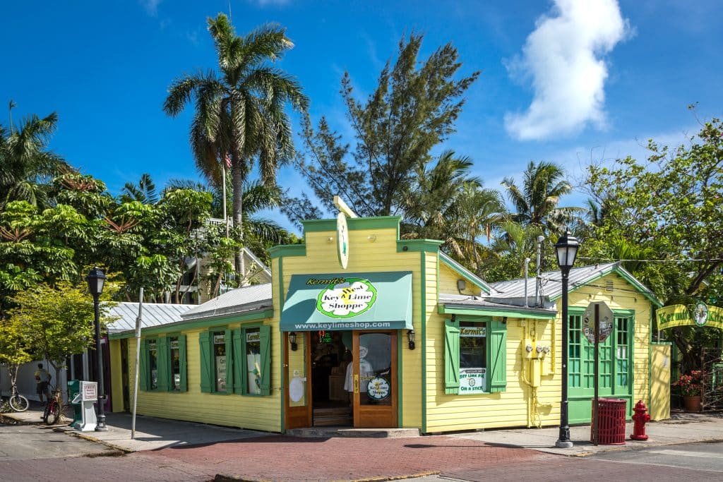 A bright yellow and green cottage with a sign reading Kermit's, surrounded by palm trees.