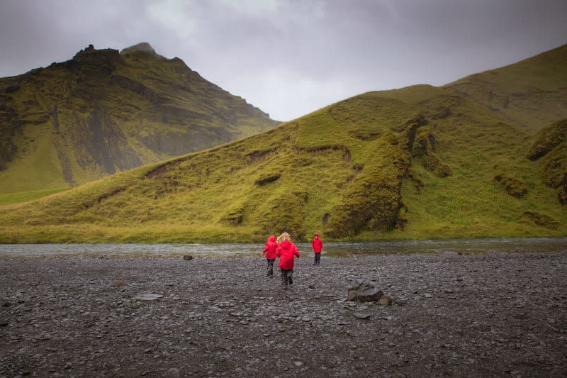kids in red raincoats running on black dirt with green hills in the background 