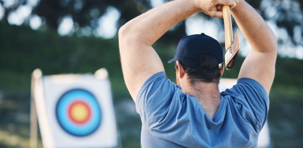 Man Axe Throwing at a Sports Range, Archery Training, or Practice with a Board Circle for Action, Game, and Fitness. Strong Person with Weapon for Tomahawk Competition, Gaming, and Park or Field with Target