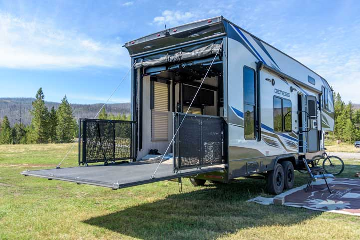 Camper toy hauler in a wooded area with the garage door open