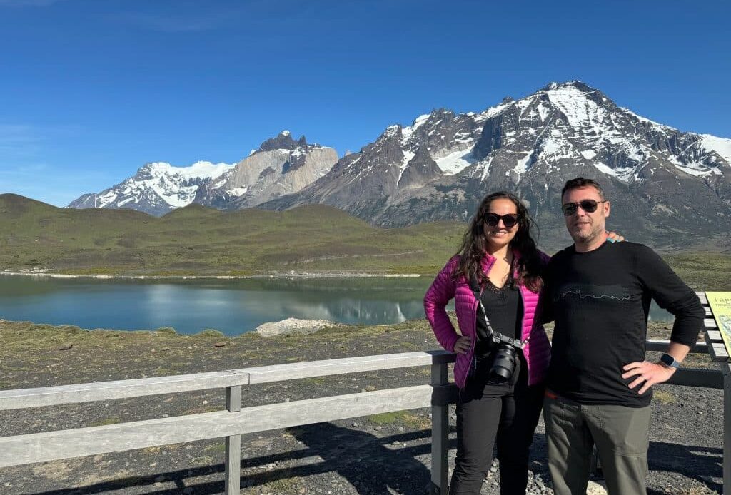 Kate and Charlie standing in front of a lake and snow-covered mountain in Patagonia.