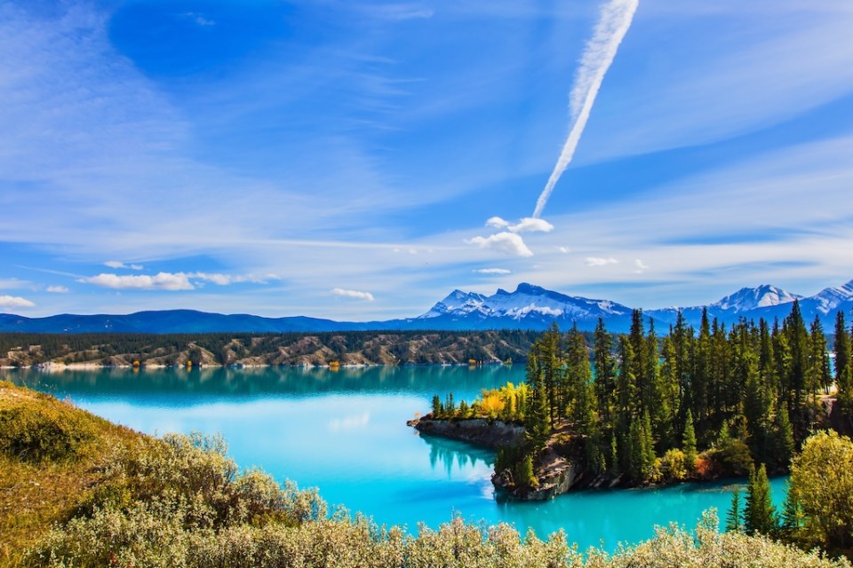 Magnificent turquoise Abraham Lake. Rocky Mountains of Canada in the Indian summer. In the blue sky silver trace of the plane.