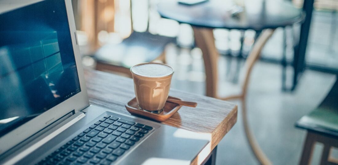A laptop and a cup of hot coffee on a wooden table in a coffee shop. 