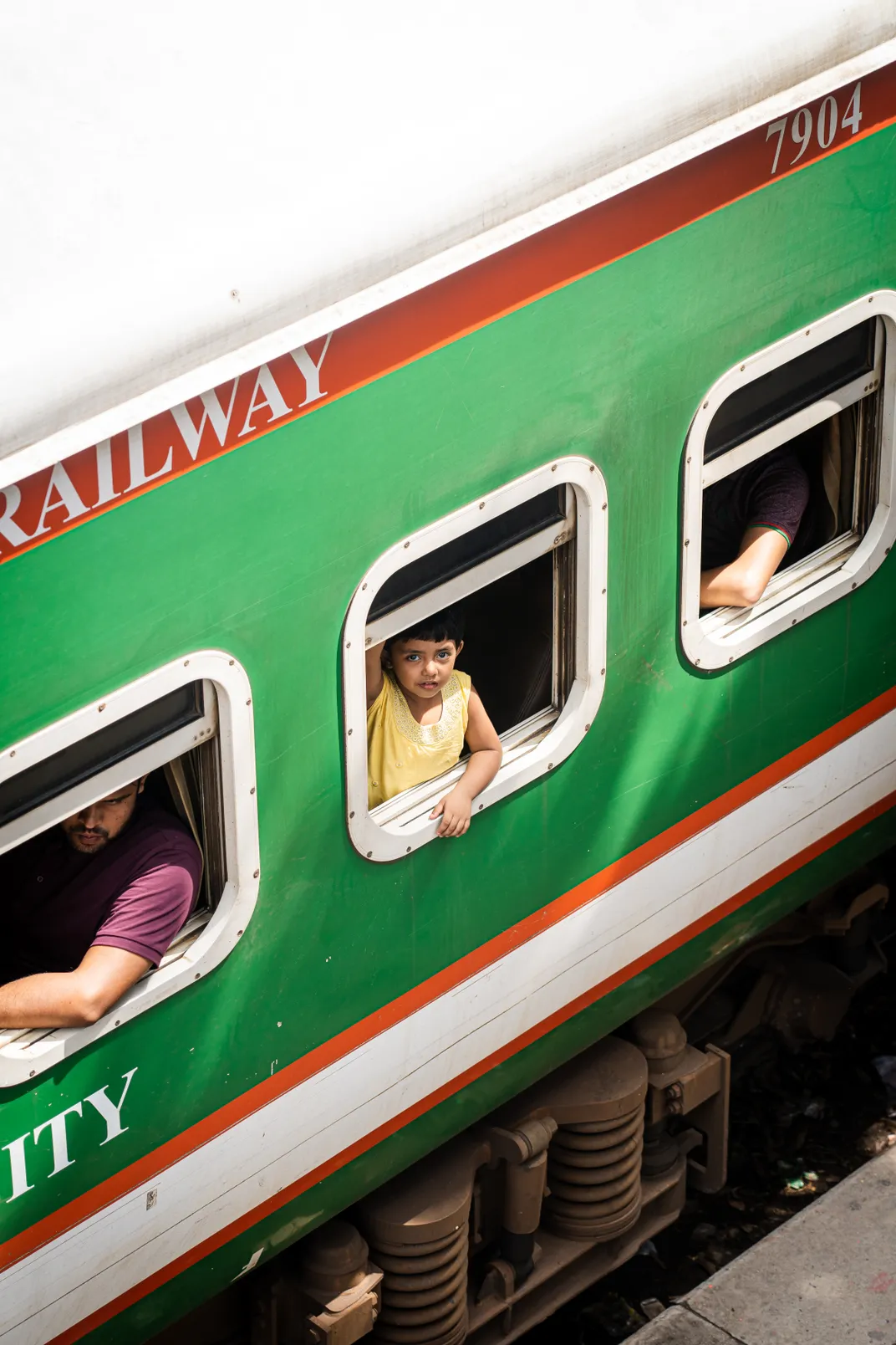 3 - A young girl traveling with her parents spots a camera while looking through the window of a train car.