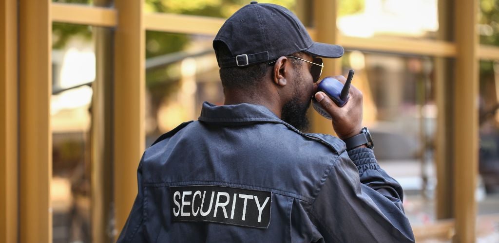 A black man wearing sunglasses and holding a walkie-talkie Security Guard Outdoors.