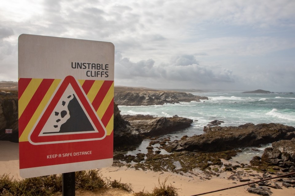 Coastline with warning cliff sign, Porto Covo, Sines, Portugal
