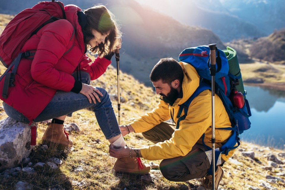 A woman has sprained her ankle while hiking, her friend uses the first aid kit to tend to the injury