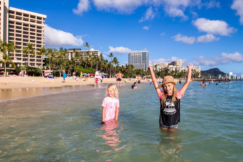 two girls holding hands up in the air in water of Waikiki beach