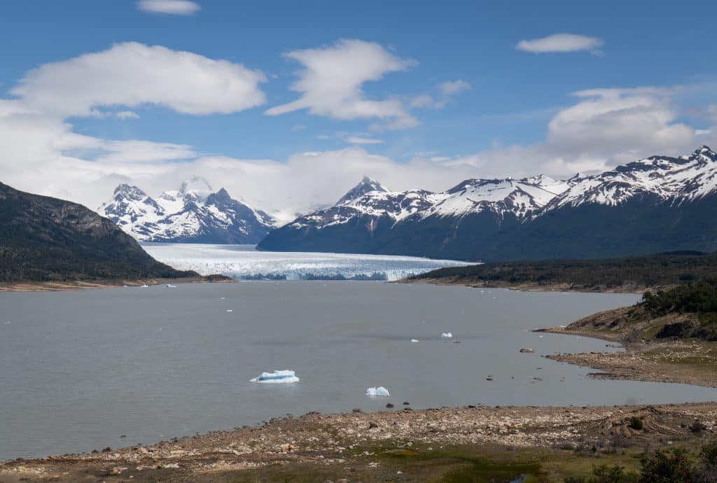 A huge white glacier in the distance, surrounded by navy blue mountains topped with streaky snow.